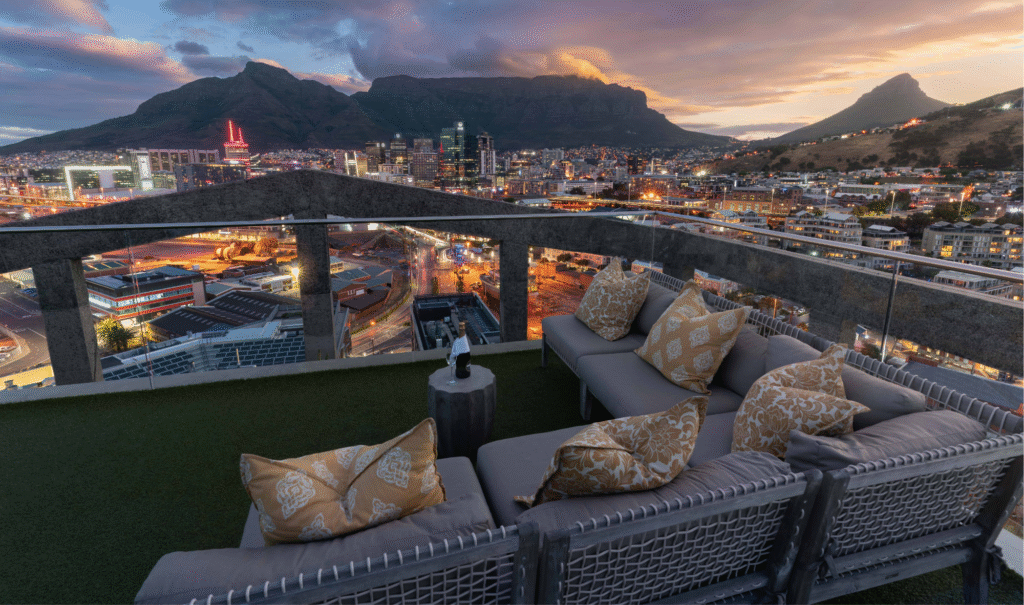 A luxurious rooftop bar overlooking Cape Town's V&A Waterfront and majestic Table Mountain at sundown, with chic seating and signature cocktails.