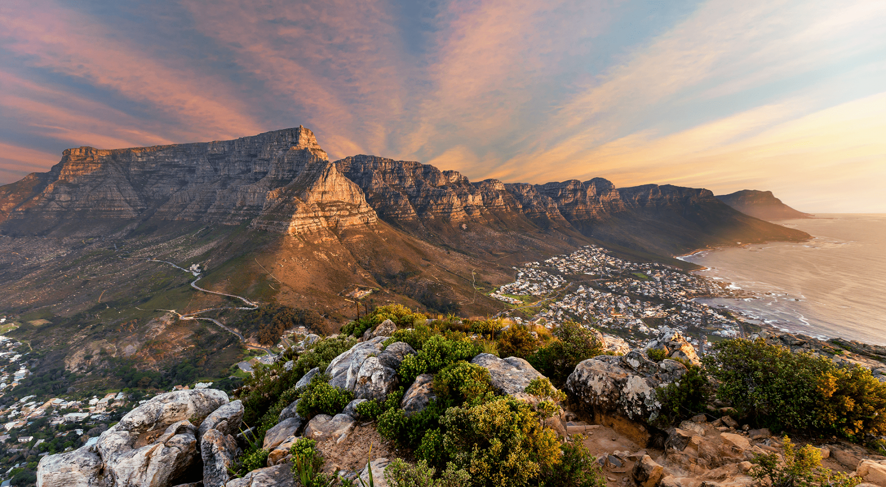 A breathtaking panoramic view of Table Mountain at sunset, with the Cape Town coastline and city below, evoking an ultimate luxury journey to South Africa.
